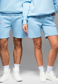 Světle modré šortky z bavlněné směsi a odpovídající mikiny, které mají pohodlný střih, žebrované manžety a malé logo v červené barvě.