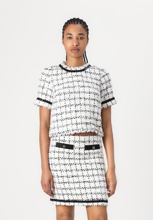 White and black tweed two-piece outfit with a cropped top and fitted skirt, featuring frayed edges and black accent detailing.