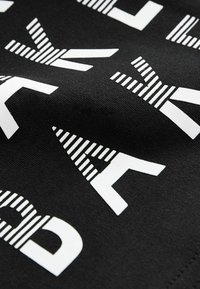 Schwarzer Stoff mit fettgedrucktem, weißem Grafiktext, der verschiedene Streifenmuster und geometrische Formen aufweist. Die Textur wirkt glatt und leicht dehnbar.