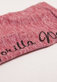 Czerwona opaska z tkaniny melanżowej o gładkiej fakturze, z czarnym napisanym kursywą napisem "Gorilla" z boku.