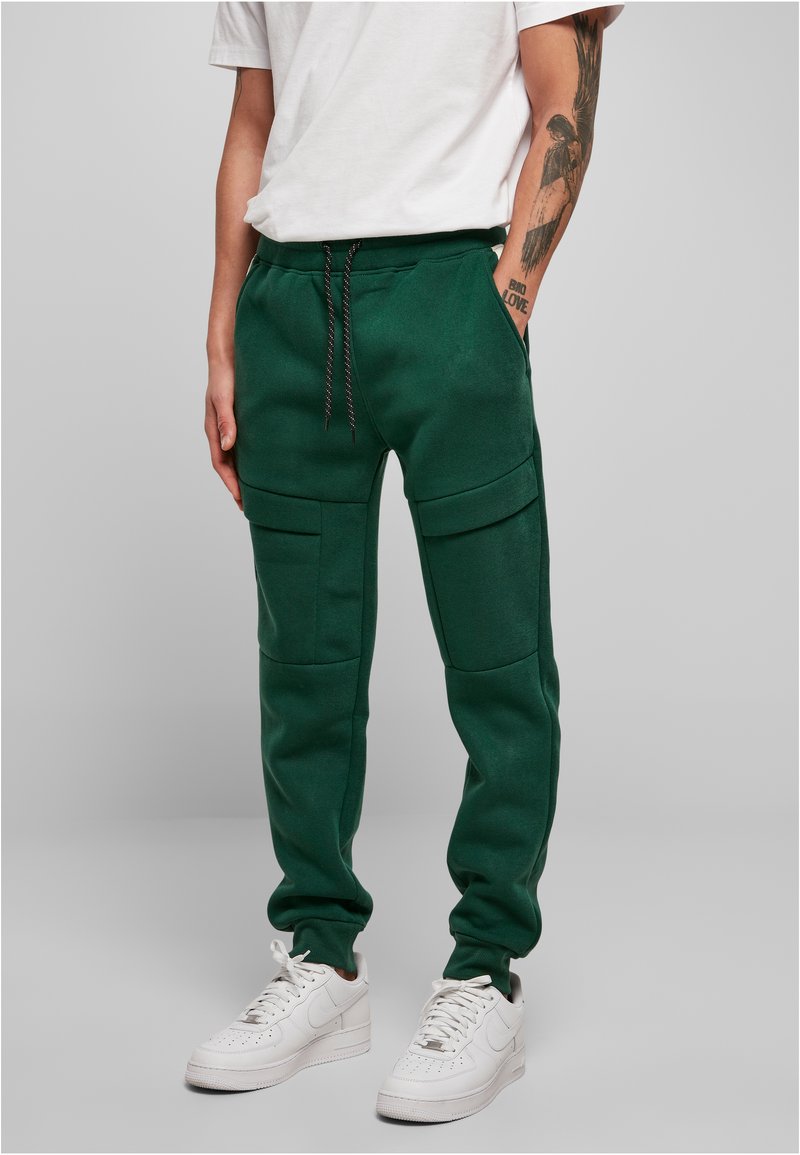 Groene sweatpants gemaakt van een zachte, gestructureerde stof. Ze hebben zijzakken en een trekkoord in de taille, gecombineerd met witte sneakers.