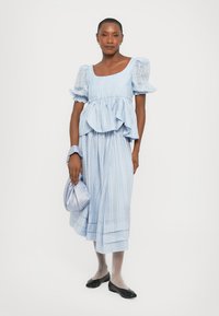Vaaleansininen raidallinen midi-mekko, jossa on puffattuja hihoja, röyhelövyötärö ja soljuva helma. Asusteena yhteensopiva satiininen clutch-laukku. Mustat ballerinat.