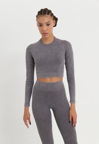 Sivi rebrasti dugih rukava crop top i visoko strukirane tajice, napravljene od teksturiranog materijala. Odjeća ima uski kroj i bešavne rubove.