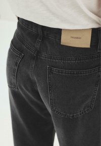 Vue arrière d'une personne portant un jean en denim noir avec des poches arrière visibles et une étiquette beige de la marque Pull&Bear sur la taille.