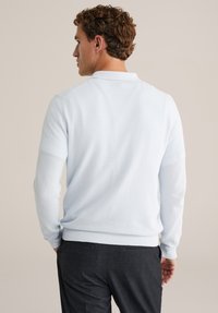 Svetlomodri pleteni pulover z teksturirano površino ter rebrastimi manšetami in spodnjim robom, kombiniran s temno sivimi hlačami.