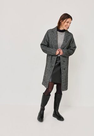 Gray textured coat with a notched collar and double buttons, layered over a gray top and a black leather skirt, paired with knee-high black boots.
