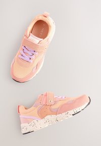 Różowe i brzoskwiniowe buty sportowe z mieszanką tkaniny i zamszu, wyposażone w pasek na rzep, lawendowe sznurowadła oraz białą podeszwę w kropki.