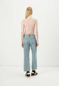 Débardeur rose clair côtelé, jean taille haute bleu clair et baskets noires et crème. Lignes épurées, coupe décontractée et détails subtils.