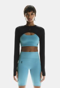 Sort langærmet top med udskæringsdesign, parret med en blå crop top og matchende blå højtaljede shorts. Glat tekstur, atletisk pasform.