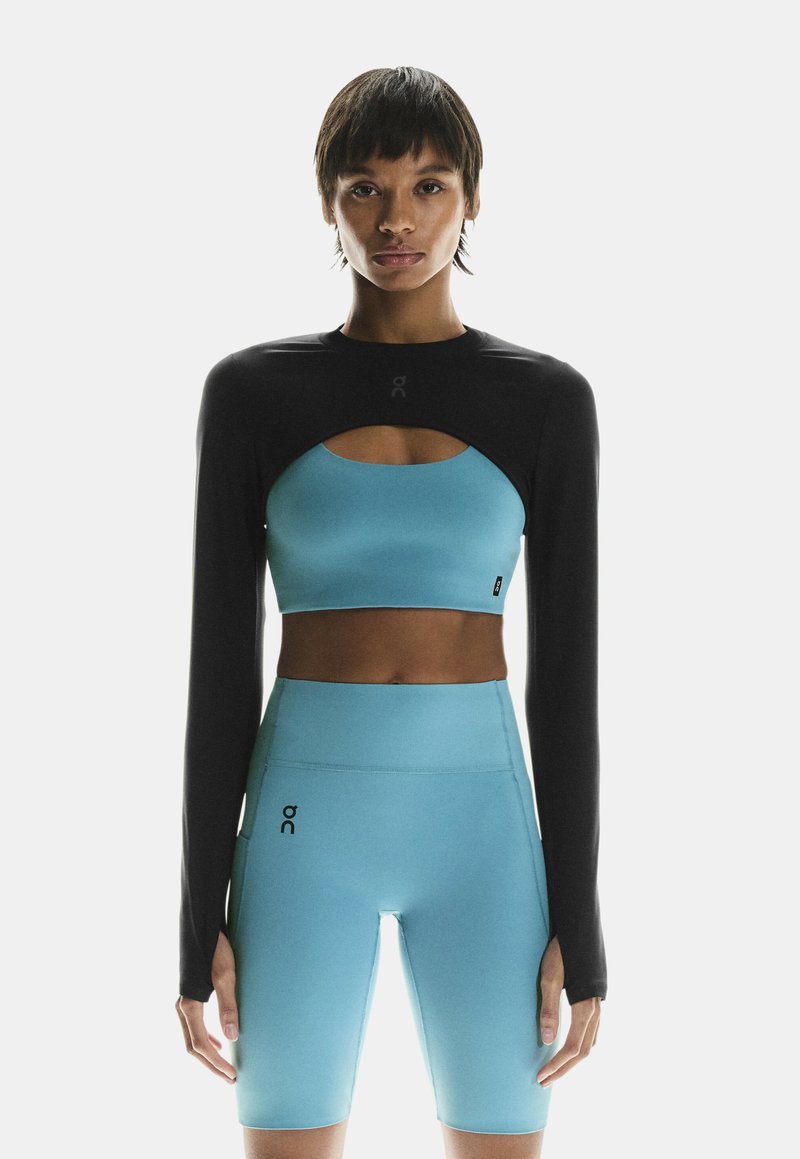 Sort langærmet top med udskæringsdesign, parret med en blå crop top og matchende blå højtaljede shorts. Glat tekstur, atletisk pasform.