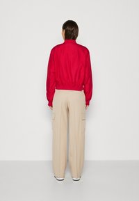 Rode bomberjack met elastische manchetten, gecombineerd met beige cargobroek met diepe zijzakken. Gladde stoftextuur, relaxte pasvorm.