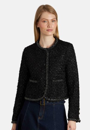 Chaqueta negra texturada con cuello redondo, bolsillos frontales y ribetes detallados, confeccionada en una tela tejida con un acabado ligeramente brillante.