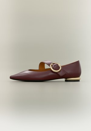 Zapato plano burdeos puntiagudo con una correa ancha y una hebilla grande dorada sobre el empeine, y un pequeño tacón con detalles dorados.
