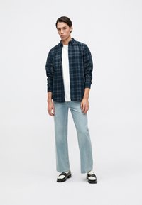 Camisa de cuadros en tonos azul marino sobre una camiseta blanca, con jeans rectos de mezclilla azul claros y zapatos en blanco y negro. Tejido suave, diseño de botonadura.