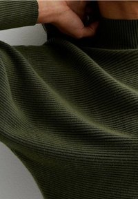 Ribattu, tummanvihreä kangas, jossa on korkea kaulus ja tekstuurilliset aallot, istuva siluetti ja sileä pinta.