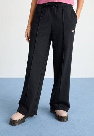 Pantalons de survêtement noirs à jambe large avec une taille élastique à cordon, poches latérales et un petit logo. Tissu lisse et coupe décontractée.