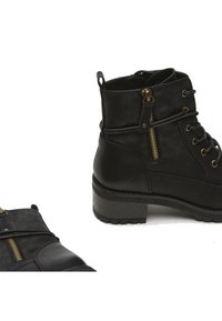 Botas tobilleras negras de cuero sintético con un acabado texturizado, que presentan detalles de cremallera y una suela de goma con diseño de tacón apilado.