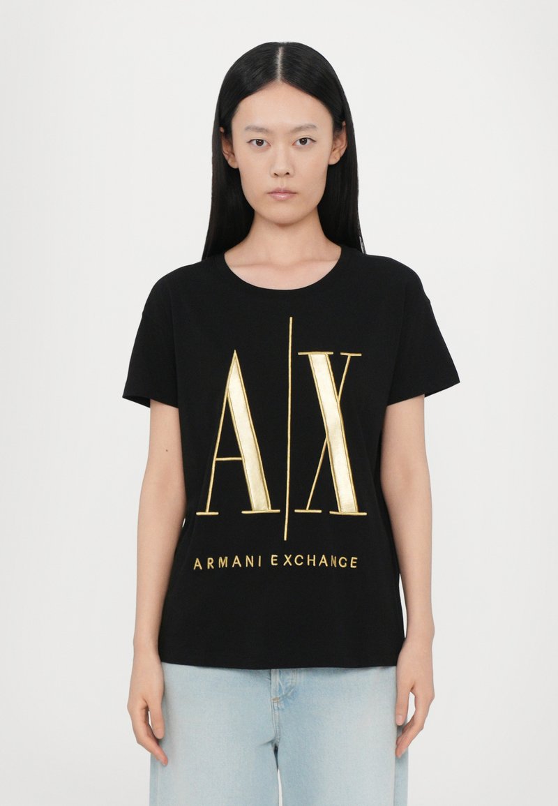 Melnā T-kreklā ar īsām piedurknēm ir liels zelta "AX" logo, kā arī zelta teksts "ARMANI EXCHANGE" apakšā. Izgatavots no kokvilnas.