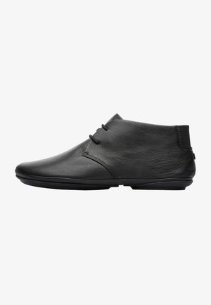 Black leather ankle boots with a smooth texture, rounded toe, and minimalistic design. Features subtle stitching and elastic accents.
