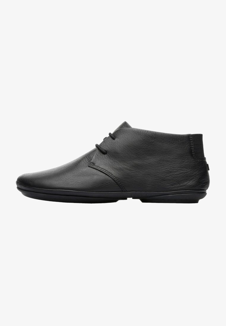 Black leather ankle boots with a smooth texture, rounded toe, and minimalistic design. Features subtle stitching and elastic accents.