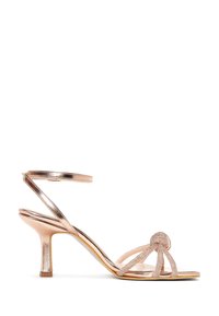 Sandalo con tacco alto color oro rosa, con cinturino alla caviglia, punta aperta, cinturini anteriori scintillanti annodati e tacco sottile di altezza media.