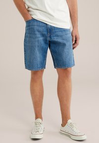 Traper šorts u srednje plavoj boji s opu�štenim krojem, s pet džepova i pojačanim šavovima. Upareni s bijelim platnenim tenisicama.