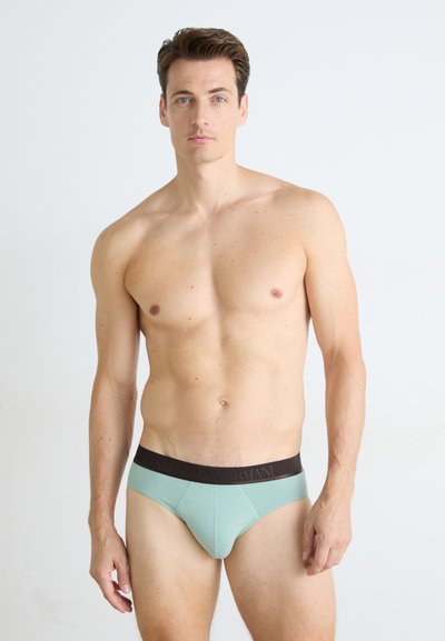 Mintgrønn truse med mørkebrun linning som har merkevarenavnet. Glatt, stretchy stoff med tettsittende design.