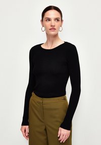 Schwarzer gerippter Langarmpullover mit Rundhalsausschnitt, kombiniert mit olivgrünen, taillierten Hosen mit seitlichen Akzenten.