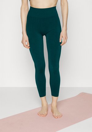 Teal high-waisted leggings in a smooth, stretchy fabric. They fit snugly and extend to the ankles, paired with a light pink yoga mat.