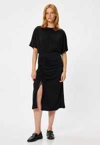 Zwarte midi-jurk met een ontspannen pasvorm, korte mouwen, geplooide zijdetails en een taille hoge split. Soepele, lichte stof.
