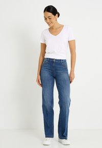 Camiseta blanca de cuello en V combinada con jeans vaqueros azules de talle alto. Los jeans presentan un corte de pierna recta y detalles sutiles de costura.