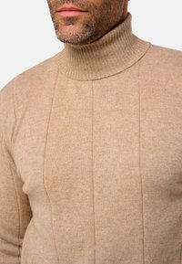 Pull col roulé beige en tricot doux, avec un col côtelé et des coutures verticales pour plus de texture et de structure.