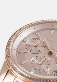 Cadran de montre en or rose avec trois petits cadrans, marqueurs d’heure en cristal et une lunette ornée de pierres précieuses transparentes.
