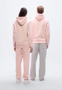 Δύο άτομα φορούν ταιριαστά φούτερ με κουκούλα: ένα ροζ και ένα γκρι. Το ροζ φούτερ έχει τσέπη καγκουρό· το γκρι παντελόνι είναι φαρδύ. Και τα δύο έχουν κουκούλες.