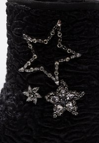 Tres decoraciones en forma de estrella, en negro y plata, adornadas con joyas, sobre una tela negra texturizada.