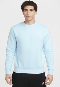 Sudadera Nike de color azul claro con cuello redondo, puños y dobladillo acanalados. Presenta un pequeño logo blanco de Nike en el lado izquierdo del pecho.