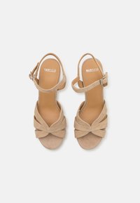 Beige suède sandalen met hakken, met een geknoopt ontwerp aan de voorkant, een verstelbare enkelband en een gladde binnenvoering met de merknaam "MANFIELD."