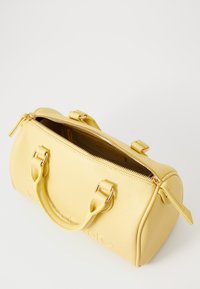 Borsa a mano in pelle gialla con superficie a ciottoli, manici doppi, hardware dorato, chiusura con zip e interno ampio. Presenta il marchio impresso sul lato.