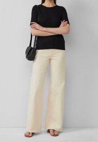 Svart t-shirt med kort ärm kombinerat med vida beige byxor och bruna sandaler. En liten svart axelväska kompletterar outfiten.