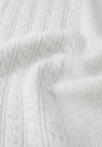 White knit fabric featuring textured cable patterns, with a cozy, soft appearance and a ribbed section, showcasing a clean and simple design.
