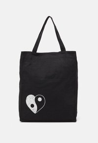 Black tote bag made of canvas, featuring a white yin-yang heart graphic. Two sturdy handles for easy carrying. Simple rectangular design.
