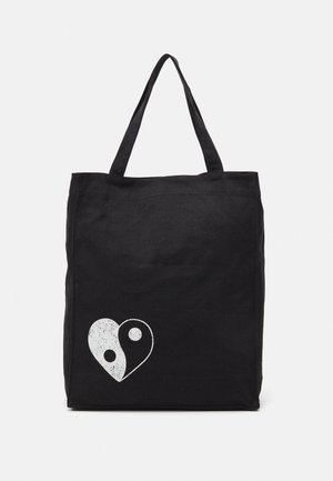 Black tote bag made of canvas, featuring a white yin-yang heart graphic. Two sturdy handles for easy carrying. Simple rectangular design.