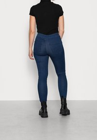 Jeans in denim blu a vita alta con un design aderente, due tasche posteriori e dettagli cuciti, abbinati a una maglietta nera a costine a maniche corte.