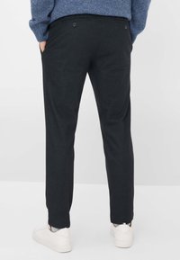 Zwarte, gebreide broek met een rechte pijp, voorzien van knopen op de achterzakken. Gecombineerd met witte sneakers en een blauwe wollen trui.