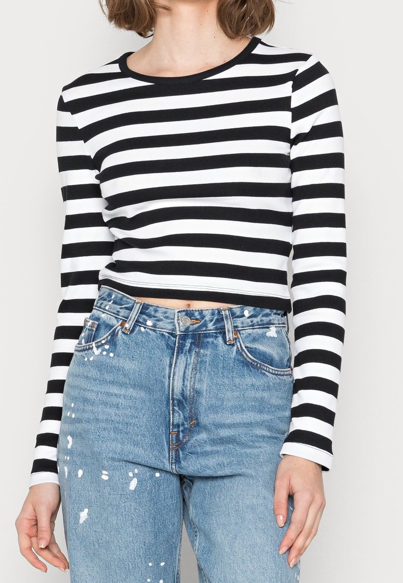 Gestreiftes langärmliges Crop-Top in Schwarz und Weiß aus weichem Material, kombiniert mit hochgeschnittenen hellblauen, stark verwaschenen Jeans.