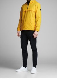Žlutá mikina s polovičním zipem, černé cargo kalhoty a bílé tenisky. Lehký materiál, elastické manžety a detail kapsy na hrudi.