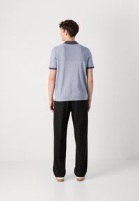 Camisa polo de manga curta azul claro com gola e punhos escuros. O tecido é texturizado, com um design ajustado. Calças pretas e sapatos claros completam o visual.