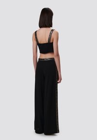 Zwart crop top van textuurstof met brede bandjes en een decoratief patroon. Geharmoniseerd met zwarte wijde broek met een accentstreep.