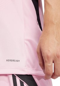 Hellrosa Sportshirt mit schwarzen Akzenten, ausgestattet mit "AEROREADY" Branding. Der Stoff wirkt glatt und feuchtigkeitsableitend, entworfen für Leistung.