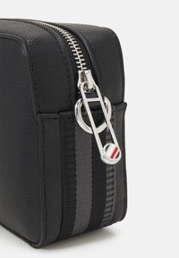 Borsa in pelle nera texture con una cerniera argentata. Presenta un accento a strisce in grigio e nero, e un dettaglio del logo sul tirante della cerniera.